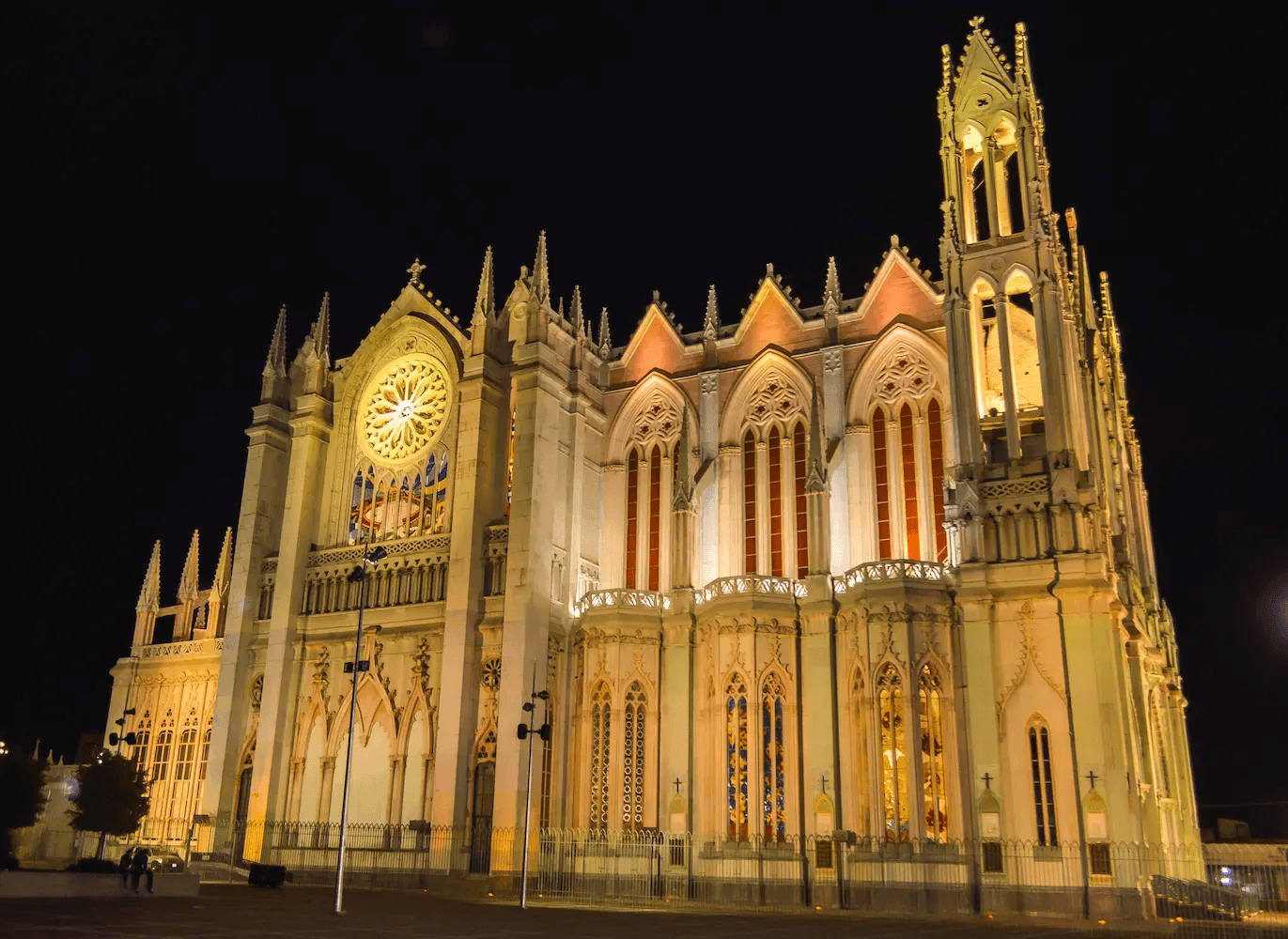 Illuminated Gothic-style cathedral at night with intricate stained glass windows and ornate architectural details.