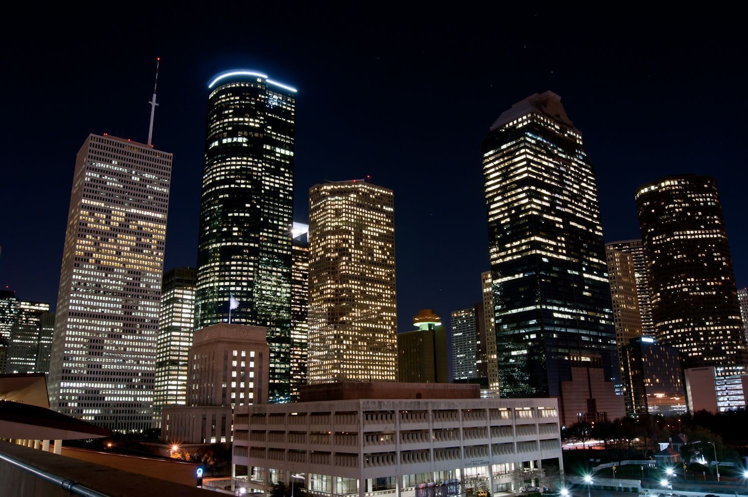 Night view of a city skyline with illuminated skyscrapers and office buildings against a dark sky.