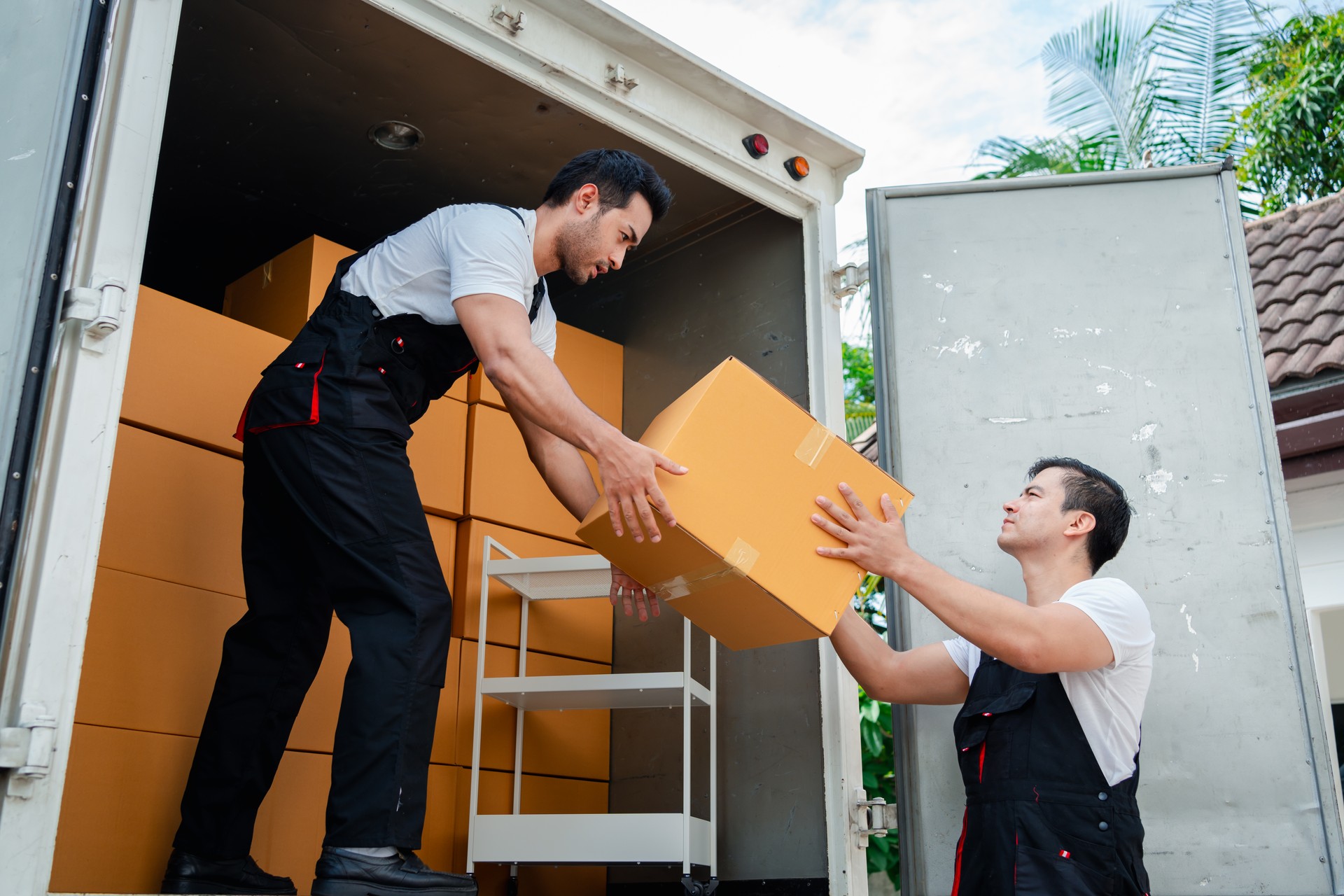 Descarga de cajas y muebles de una camioneta a una nueva casa con servicio de carga de dos hombres trabajadores de mudanzas en cajas de elevación uniformes. concepto de mudanza y entrega a domicilio.